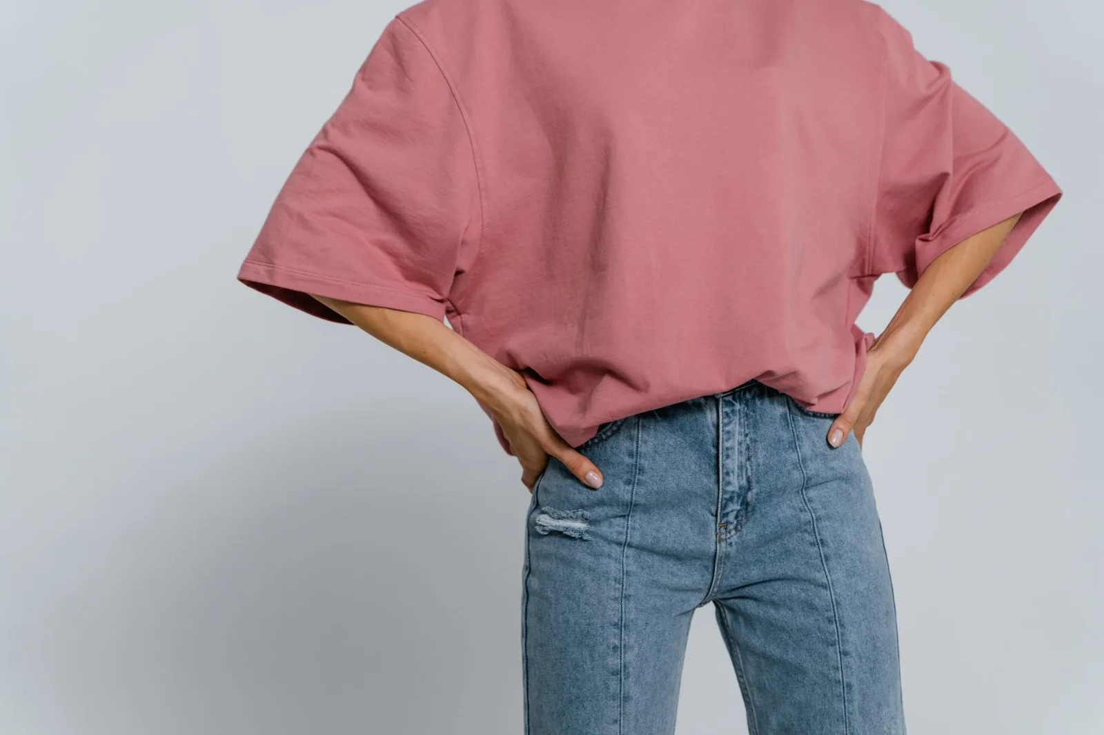 A person wearing an oversized T-shirt tucked at the front with straight-leg jeans